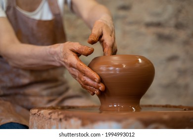 Sculptor In The Studio Makes A Clay Pot Close-up. Senior Woman Is Sculpting A Bowl Behind A Rotating Potter's Wheel