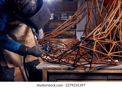 Sculptor is using arc welding to assembly metal sculpture in protective mask