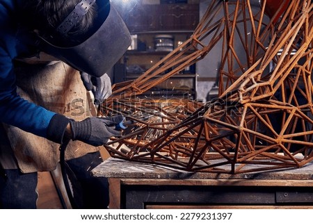 Sculptor is using arc welding to assembly metal sculpture in protective mask