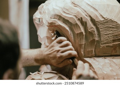 Sculptor is using a mallet and chisel to carve a large piece of wood in a workshop, with wood chips flying through the air
