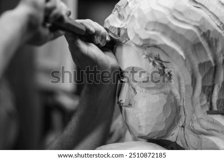 Sculptor is using a mallet and chisel to carve a large piece of wood in a workshop, with wood chips flying through the air