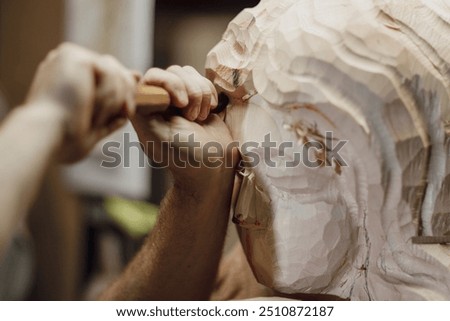 Sculptor is using a mallet and chisel to carve a large piece of wood in a workshop, with wood chips flying through the air