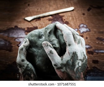 Sculptor's Hands Modelling A Block Of Clay On A Wooden Table