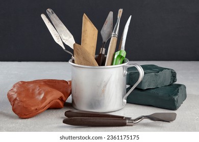 Sculptors tools in a metal mug and pieces of clay and plasticine on a black background. Tools for creative sculpting on a table in a workshop. - Powered by Shutterstock