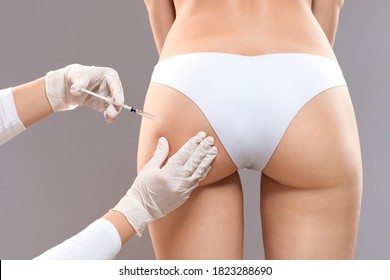 Sculptra butt lifting concept. Slim woman having hip injection at beauty salon, closeup. Plastic surgeon making injection at butt area for unrecognizable lady, grey studio background, back view
