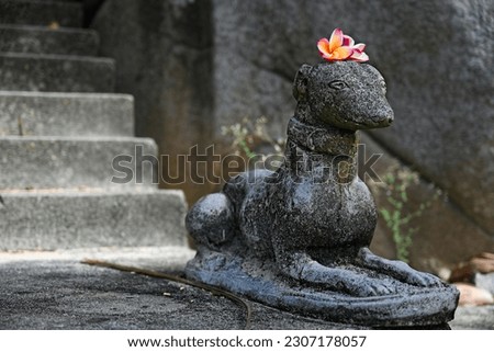 Sculpture of a dog with plumeria flowers placed on its head.