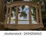 A sculpture in the form of a Greek theatre provides a window through the trees over Lake Maitland in Winter Park, Florida. Black and white.