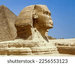 Sculpture of the Great Sphinx against the blue sky. Profile view. The head, part of the body and the top of the ancient pyramid above the back are visible. Egypt. Giza