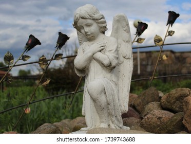 sculpture of a little angel against a gloomy sky and metal roses