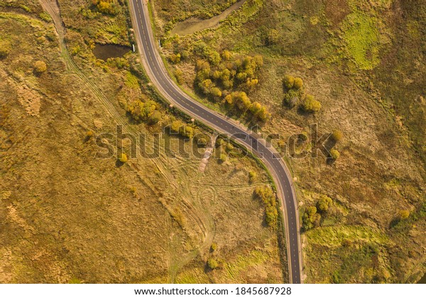 S-curved road goes through the flat ground with\
meadows, bushes and trees in autumn colours. Top-down view. No\
cars, no people.