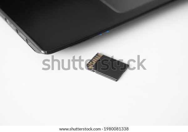SD memory card\
next to a new modern laptop on a white table. Side View - Focus on\
the media card reader drive.