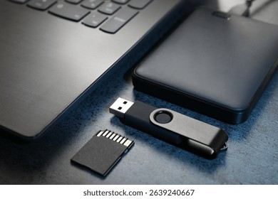 SD memory card, USB flash drive, hard disk drive and laptop on dark grey table, closeup