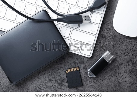 SD memory card, USB flash drive, hard disk drive with cable and keyboard on dark grey table, flat lay
