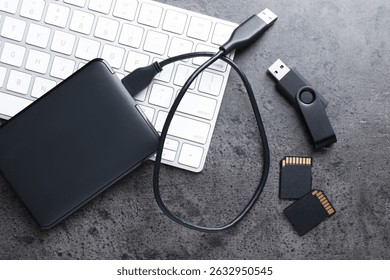SD memory cards, USB flash drive, hard disk drive with cable and keyboard on dark grey table, flat lay