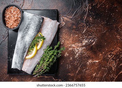 Sea Bass fillets, Raw Seabass fish with thyme, pink salt and lemon on marble board. Dark background. Top view. Copy space.