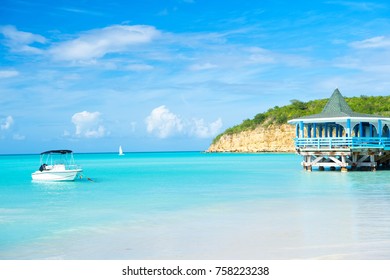 Sea Beach With Boat And Wooden Shelter On Turquoise Water In St Johns, Antigua On Blue Sky Background. Summer Vacation On Caribbean. Adventure, Travelling, Wanderlust Concept