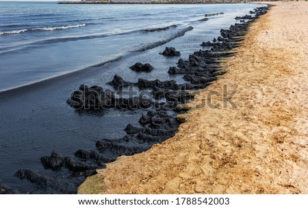 The sea and the beach are polluted with oil. A crude oil spill on the sand of a city beach. Beach oil spill impact, pollution, waste disposal. Ecological catastrophy. Selective focus