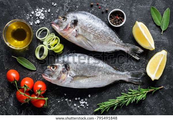 Sea\
bream or dorado sea fish, olive oil, spices herbs and cooking\
ingredients on dark slate background. Top view. Mediterranean\
cuisine, healthy eating, healthy cooking\
concept