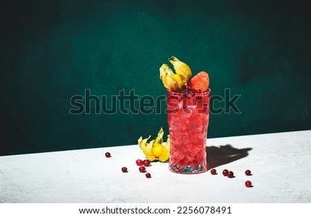 Sea breeze alcoholic cocktail with vodka, cranberries, grapefruit juice, orange and ice, decorated with physalis. Dark green background, hard light and shadow pattern