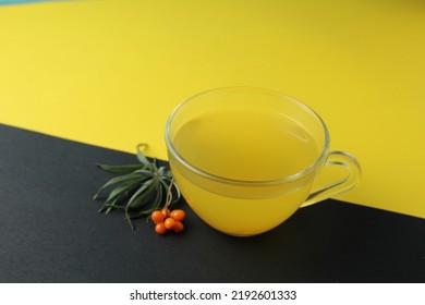 Sea Buckthorn Tea Drink On A Black Yellow Bright Background. Sea Buckthorn Drink Tea Juice In A Glass Cup Next To A Spout Of Sea Buckthorn Leaves Orange Berries On A Black And Yellow Background. 