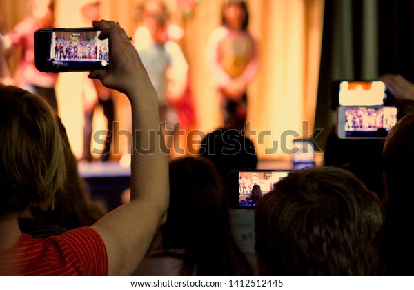 A sea of\
parents’ cell phones are held high to record their children’s\
performance in a school play.