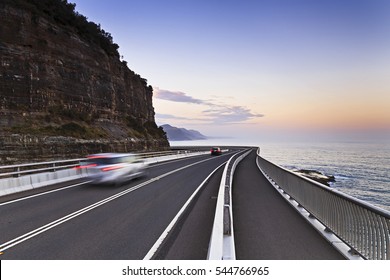 Sea Cliff bridge of Grand Pacific Drive along the NSW coast of Australia on Pacific at sunset. Scenic tourist drive with blurred cars around cliff road bend.