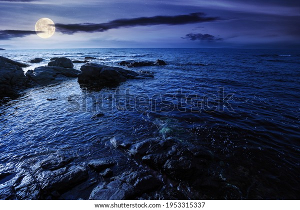 sea coast scenery at night. boulders in the\
calm water. few clouds on the sky in full moon light. lonely place\
for summer vacations. sunny\
weather