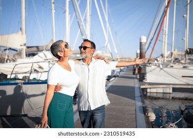 Sea Cruise Offer. Senior Husband Hugging Wife And Showing Their New Yacht In Marina, Gesturing With Hand Inviting Lady On Luxury Summer Adventure. Happy Mature Couple Posing At Dock Outdoor - Shutterstock ID 2310519435