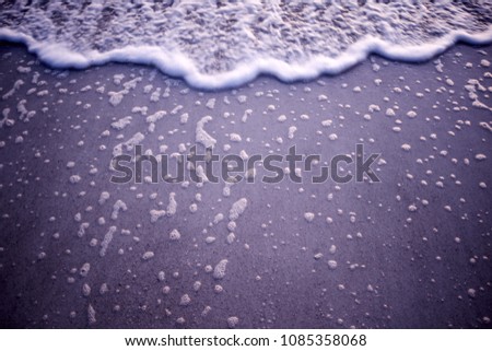 Sea foam border with stranded bubbles on wet beach sand as the tide ebbs and flows on Anna Maria Island, Florida with vignette and glow of the setting sun