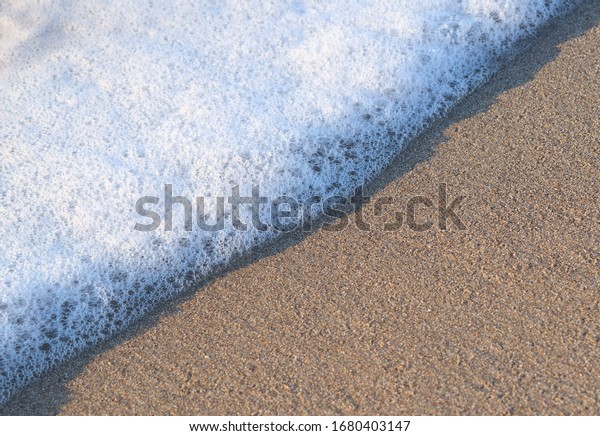 Sea foam on the seashore. Photo diagonally\
divided in half. Sea foam and sand. There is a place for text.\
Beach season. Summer. Holiday\
season.