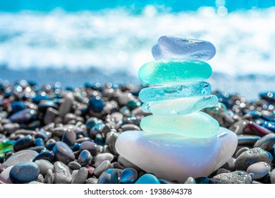 Sea glass stones arranged in a balance pyramid on the beach. Beautiful azure color sea with blurred seascape background. Meditation and Harmony concept