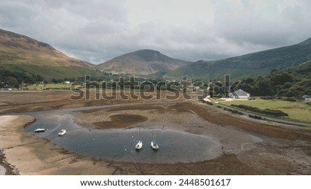 Sea gulls flying at brown sand beach on ocean shore aerial. Nature seascape with historical ancient castle ruins. Seagulls bird at summer cloudy day. Ships, yachts at harbor of Arran Island, Scotland