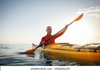 Sea kayaking. Senior man paddling kayak on the sunset sea. Acitve vacation, kayaking, paddling, canoeing - Powered by Shutterstock