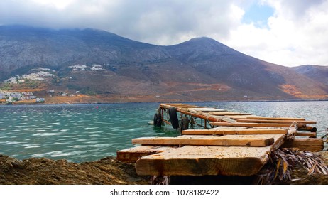 Sea Landscape With A Wooden Diving Board In Front Of The Bay And A White Greek Village On The Other Side Of The Mountain