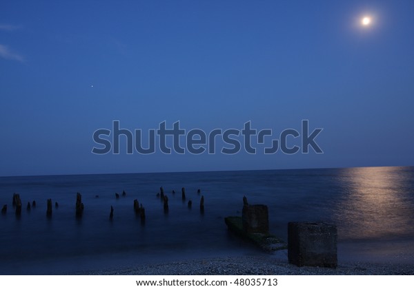 Sea at night with\
moon and wooden poles