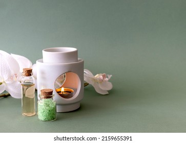 Sea salt for baths and body oil on a green table. A tea candle in a candlestick and a sprig of white orchid in the background. Light green background, place for text