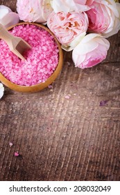 Sea salt in bowl with roses on wooden background. Top view, copy space.