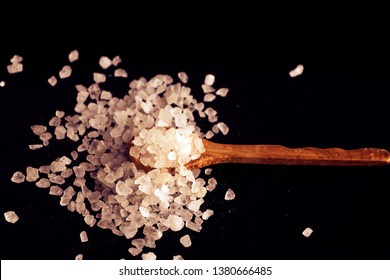 Sea salt and microbead plastic particles in wooden spoon on black background. Copy space.