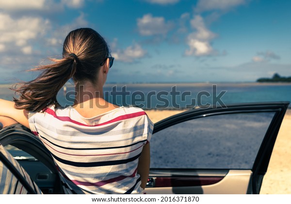 Sea side vacation road trip.\
Female traveler relaxing by her car looking out to the\
sea.