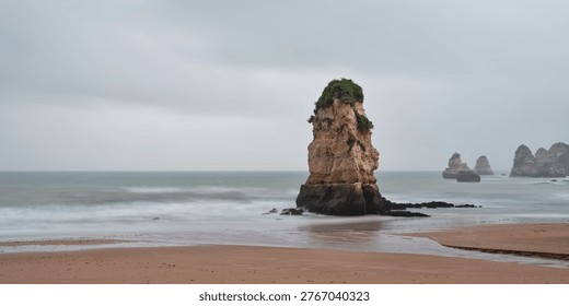 Sea stack on a sandy beach in Lagos Algarve Portugal with calm ocean water and overcast sky forming a panoramic coastal landscape and travel background
