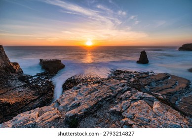 A sea stack rises from the Pacific Ocean at Davenport Beach, California, as soft waves and warm sunset light reflect on wet sand, creating a calm and scenic coastal view