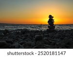 Sea stones standing on top of each other against the backdrop of a sunset on the seashore.