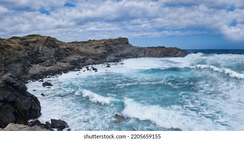 a sea with strong swell beating against the walls of a rocky cliff, blue rough sea with big waves with foam crashing against the rocks, Menorca, Balearic Islands, Spain