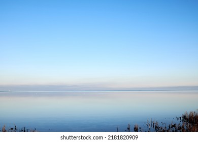 Sea at sunset with clear blue sky making a nature mirror reflection on the water with golden grey clouds on the horizon at dusk. Copy space, wallpaper background of beautiful and colorful ocean view