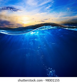 Sea water design template with underwater part and sunset skylight splitted by waterline. Water with air bubbles in sunlight