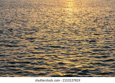 Sea Water At Sunset Background. Ocean Surface Small Ripples, Orange Reflections. Summer Vacation Empty Backdrop