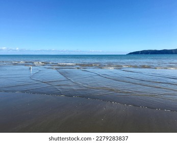 Sea wave interference pattern on flat Paraparaumu beach with Kapiti Island in the background. 