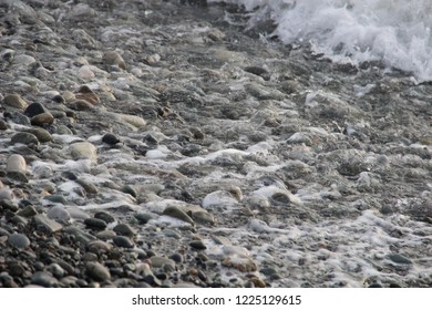 the sea wave running on the pebble beach in the evening