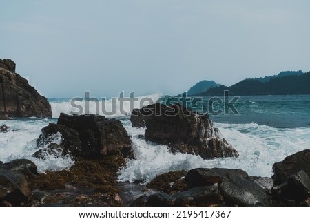 Sea waves hitting rocks in a beautiful beach with mountain background.
