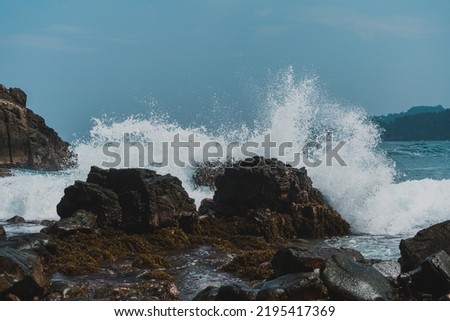 Sea waves hitting rocks in a beautiful beach with mountain background.